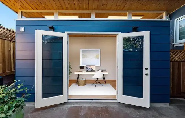 Backyard office ADU in Oakland with navy siding, white French doors and a wood ceiling over the entry