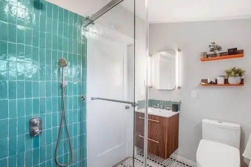 Berkeley bathroom remodel with teal glossy wall tile, frameless glass shower, walnut vanity and floating orange shelves
