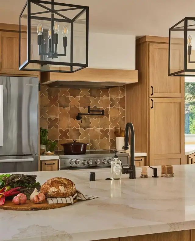 Kitchen remodel by HDR Remodeling with warm wood cabinets, black lantern pendants and a patterned tile backsplash behind the range
