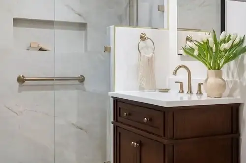 Albany bathroom remodel with large marble-look tile, a brass grab bar in the shower, dark wood vanity and brass faucet