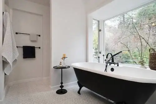 Oakland primary bathroom with a black clawfoot tub, hex tile floor and a large window onto trees