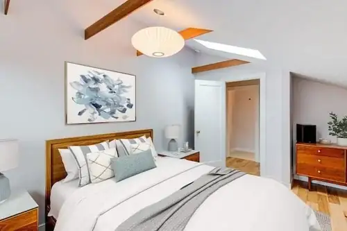 Oakland attic conversion bedroom with exposed wood beams, a skylight, a paper pendant lamp and a wood bed frame